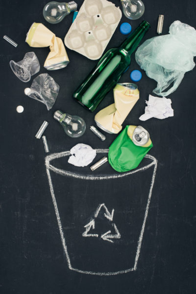 various types of trash falling into drawn trash can with recycle sign on chalkboard