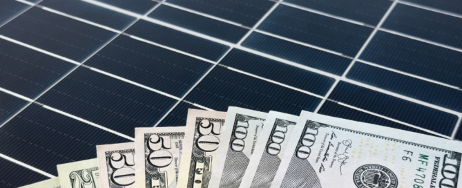 A close-up of U.S. dollar bills fanned out on top of a solar panel.