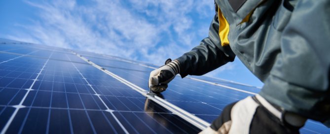 Technician installing solar panels under a clear blue sky, representing Sunergy Systems' professional solar panel installation services.